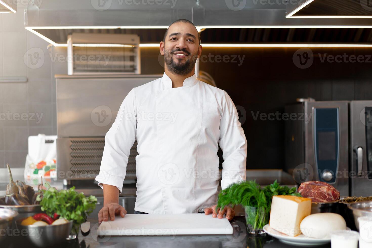 bello giovane africano capocuoco in piedi nel professionale cucina nel ristorante preparazione un' pasto di carne e formaggio verdure. foto