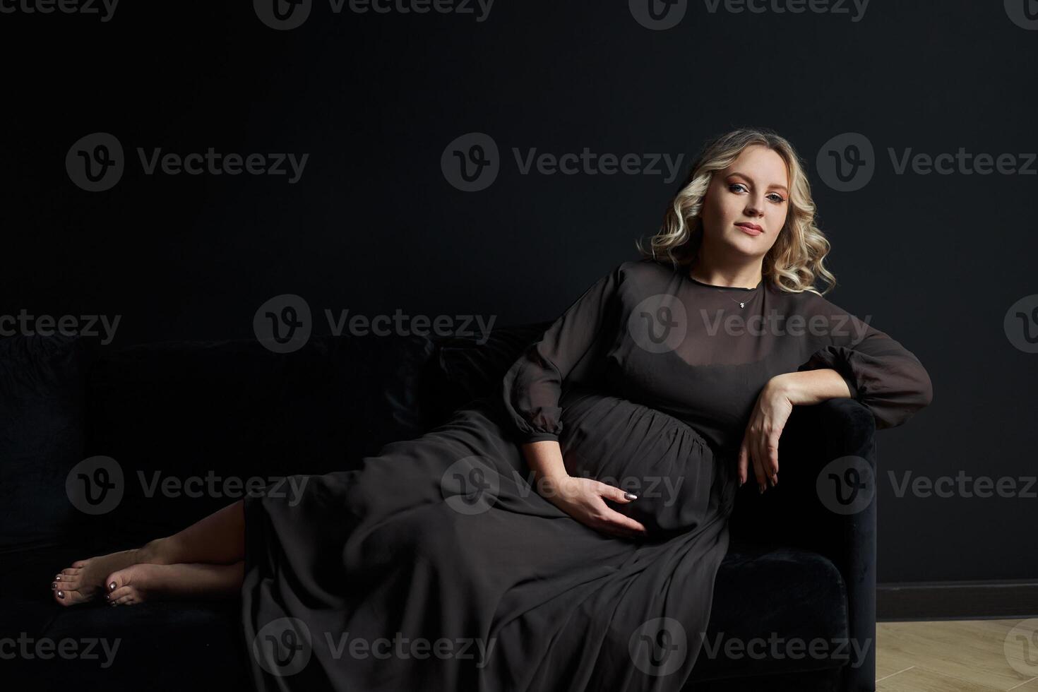 incinta donna in posa nel un elegante nero vestito in casa studio nero parete sfondo foto