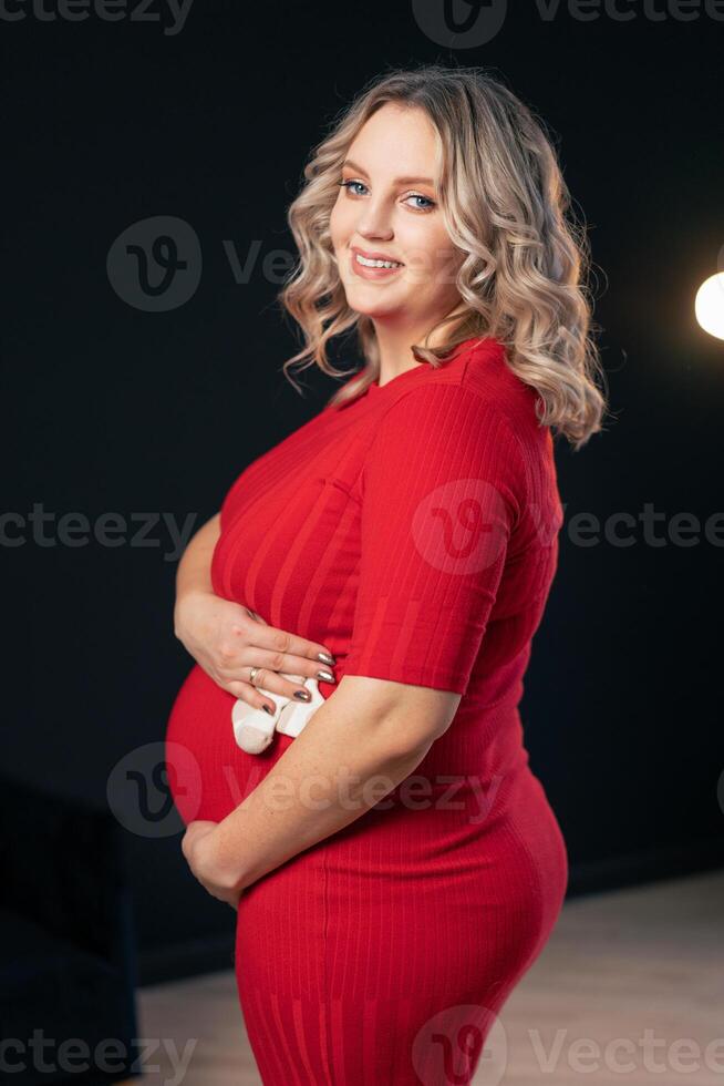 incinta donna in posa nel un elegante rosso vestito in casa studio nero parete sfondo foto