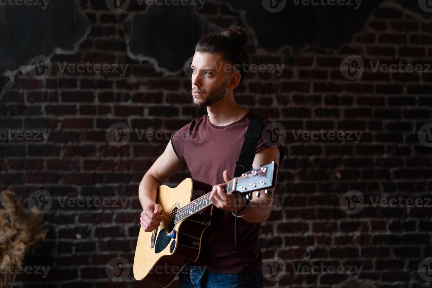 uomo con acustico chitarra contro mattone parete giocando musica cantando canzoni godere vita medio sparare foto