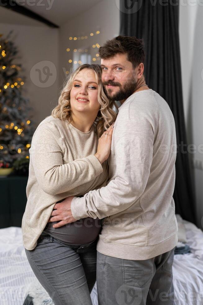 contento famiglia concetto. marito abbraccio pancia incinta moglie in piedi interno vivente camera vicino divano foto