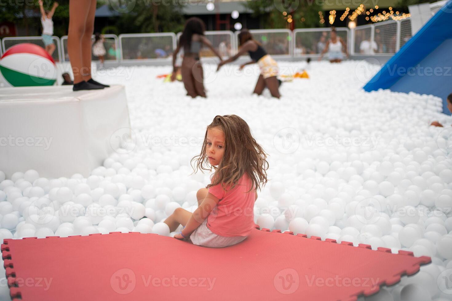 contento poco ragazza giocando bianca plastica palle piscina nel divertimento parco. foto