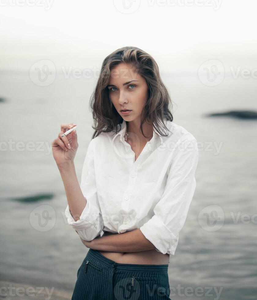 carino donna fuma un' sigaretta su il spiaggia foto