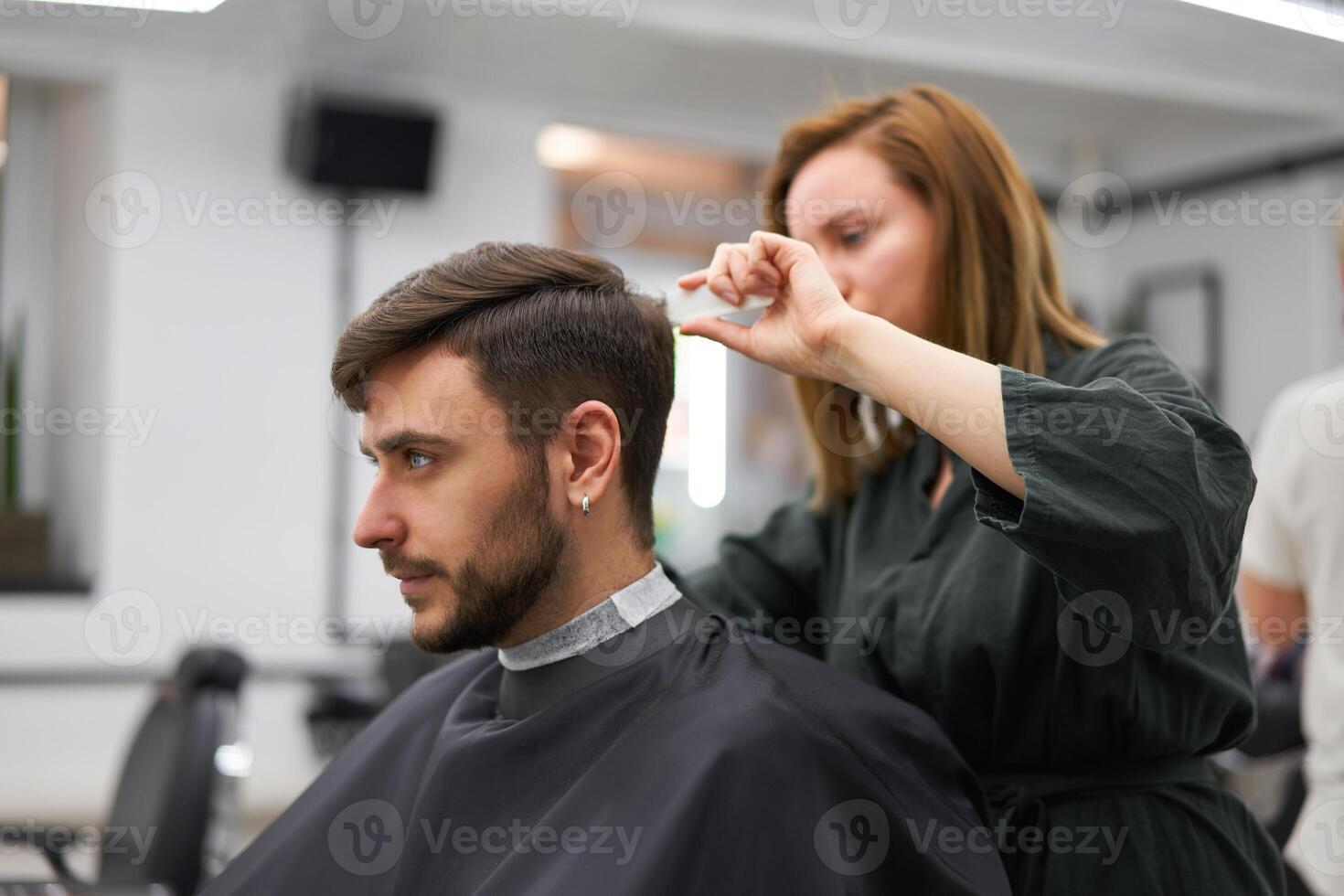 bello blu con gli occhi uomo seduta nel barbiere negozio. parrucchiere parrucchiere donna taglio il suo capelli. femmina barbiere. foto