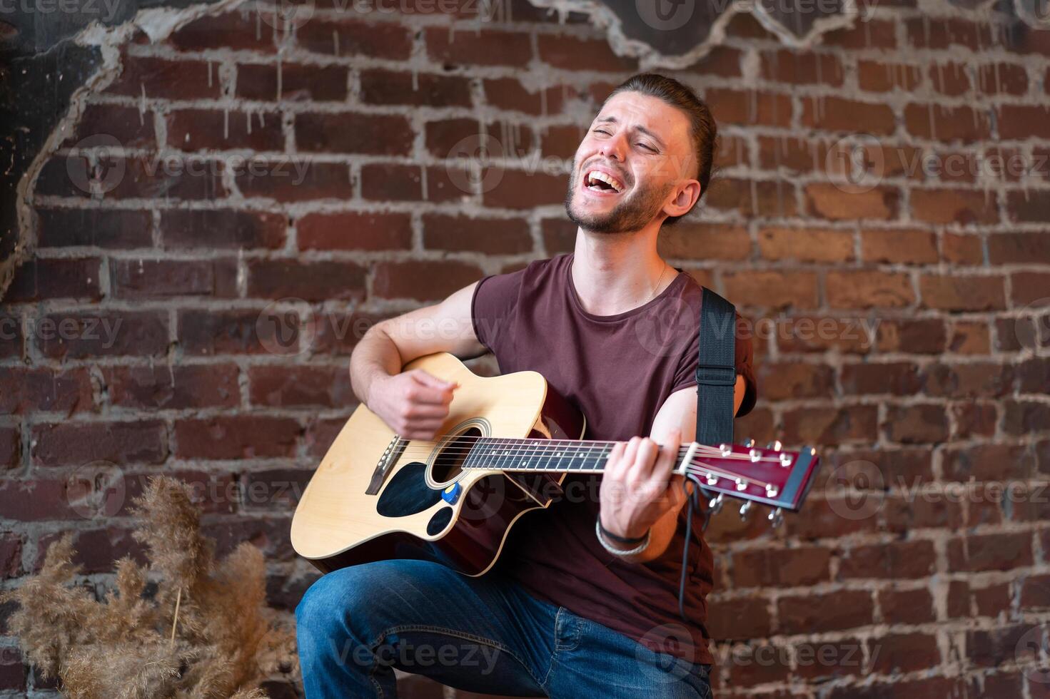 uomo con acustico chitarra contro mattone parete giocando musica cantando canzoni godere vita medio sparare foto