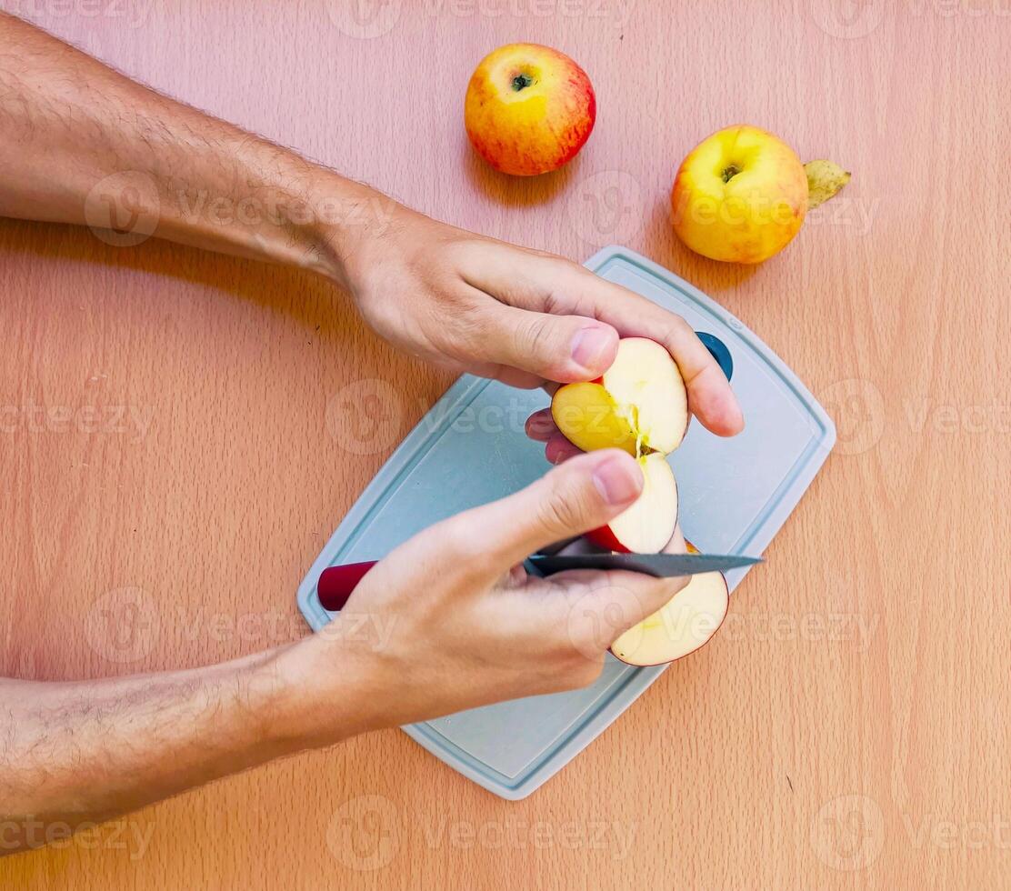 vicino su maschio mani tagliare un Mela in fette. superiore Visualizza di preparazione frutta al di sopra di cucina tavolo. foto