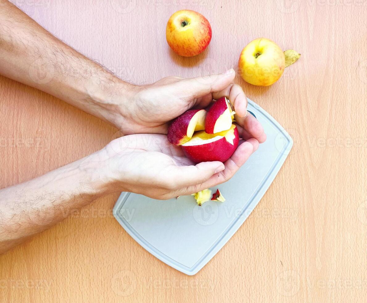 vicino su maschio mani tagliare un Mela in fette. superiore Visualizza di preparazione frutta al di sopra di cucina tavolo. foto