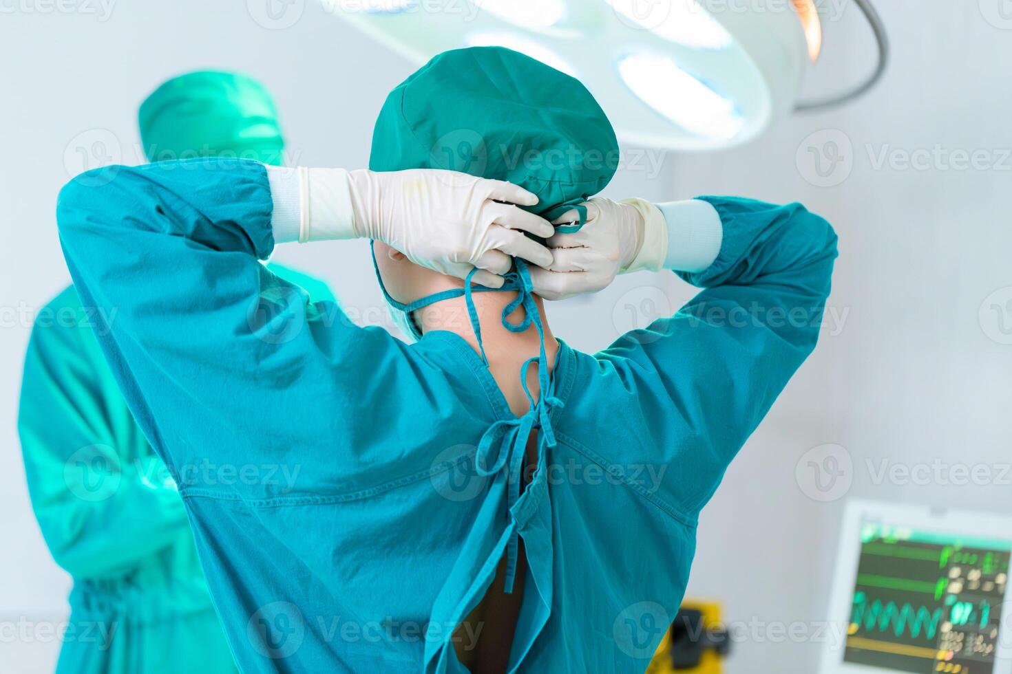 chirurgo di squadra al lavoro in sala operatoria, vista posteriore del chirurgo che lega il cappuccio chirurgico in preparazione, squadra medica che esegue un intervento chirurgico in sala operatoria foto