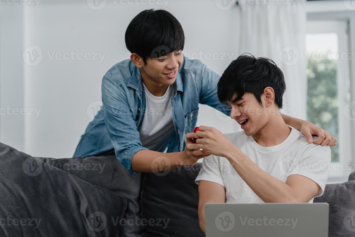 giovani coppie gay asiatiche propongono a casa moderna, adolescenti coreani lgbtq uomini sorridenti felici hanno tempo romantico mentre propongono e sorpresa di matrimonio indossano l'anello nuziale nel soggiorno al concetto di casa. foto