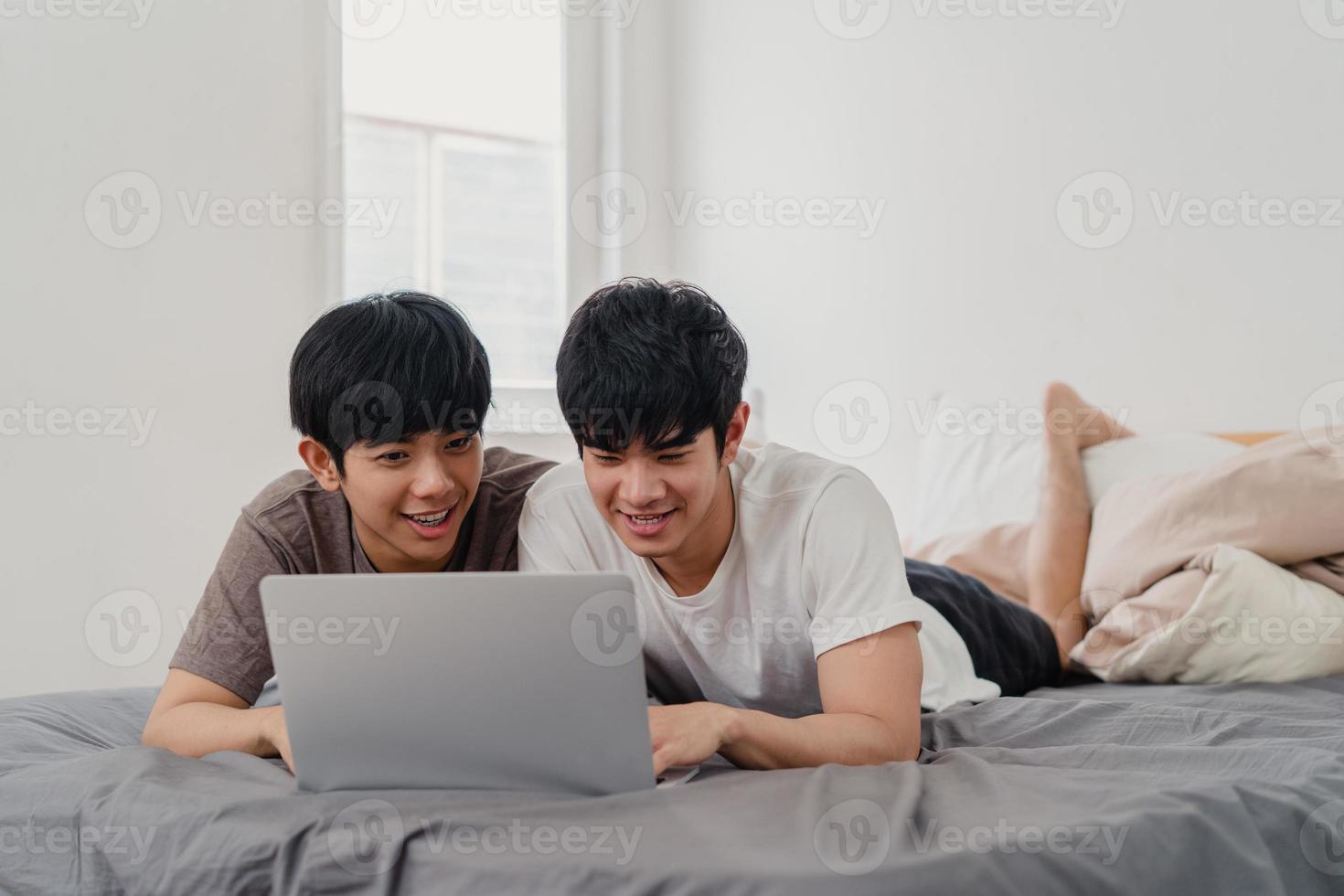 coppia di uomini gay lgbtq asiatici utilizzando il computer portatile a casa moderna. giovane amante dell'asia maschio felice rilassarsi riposare insieme dopo il risveglio, guardare film sdraiato sul letto in camera da letto a casa al mattino concetto. foto