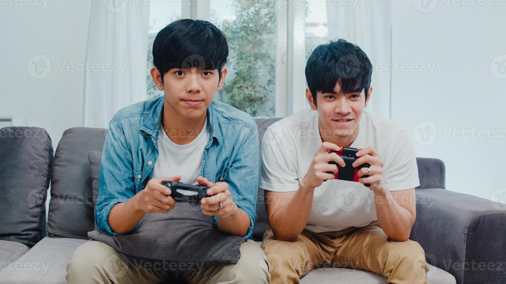 giovani coppie gay asiatiche giocano a casa, adolescenti uomini lgbtq coreani che usano il joystick che hanno un momento felice e divertente insieme sul divano nel soggiorno di casa. foto