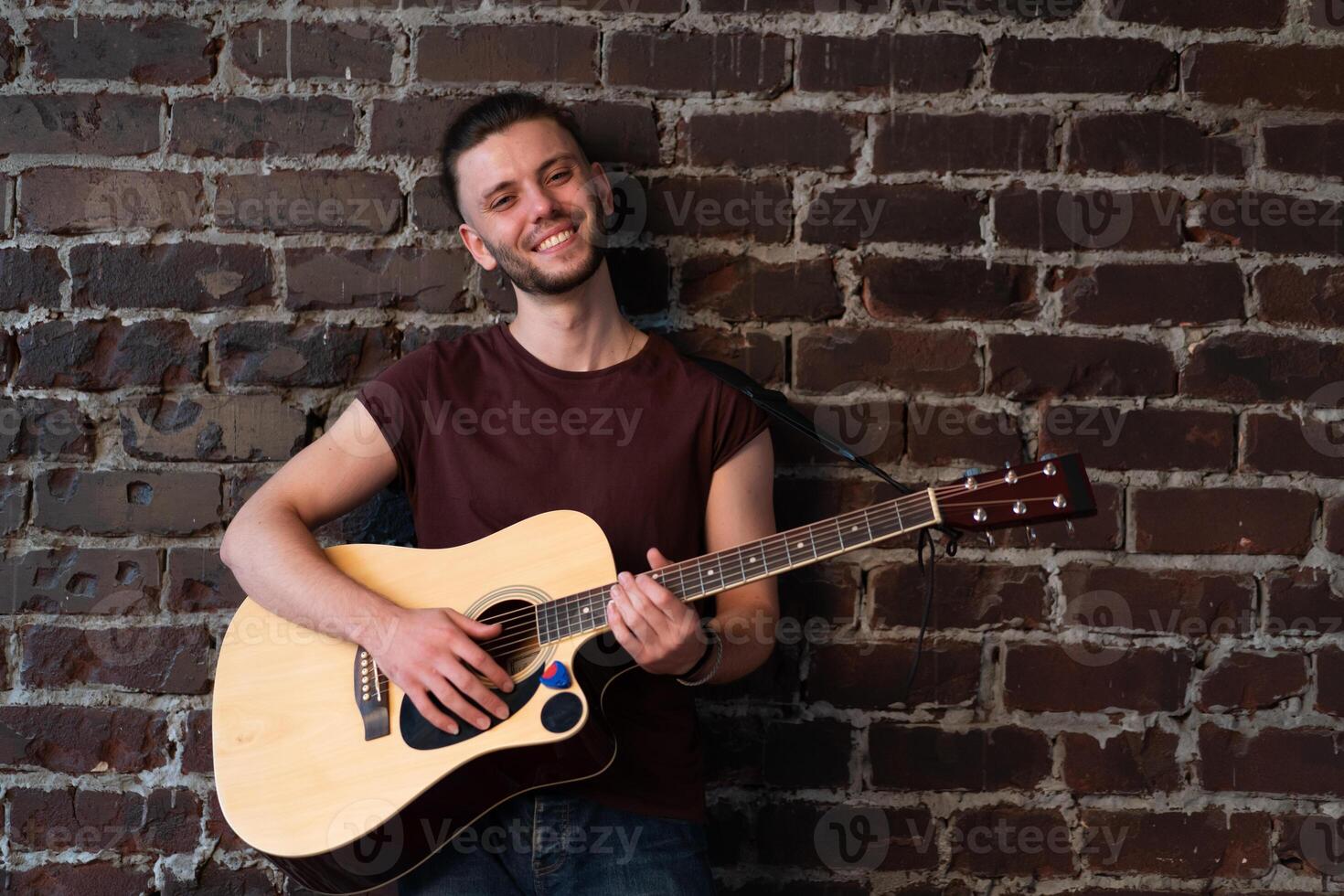 uomo con acustico chitarra contro mattone parete giocando musica cantando canzoni godere vita medio sparare foto