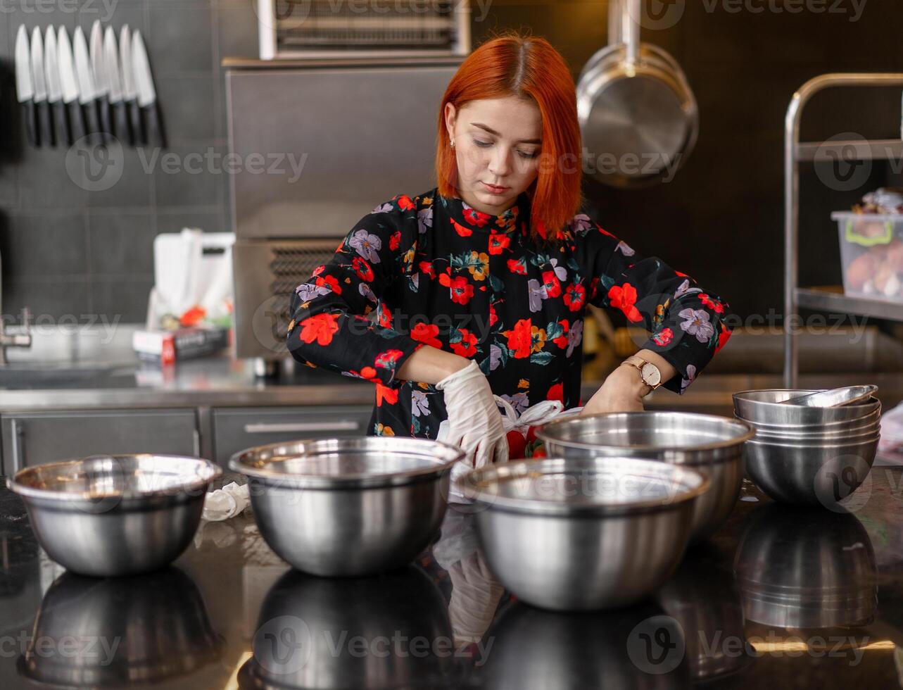 bellissimo giovane dai capelli rossi ragazza nel sera vestito è preparazione cibo nel un' professionale cucina. foto
