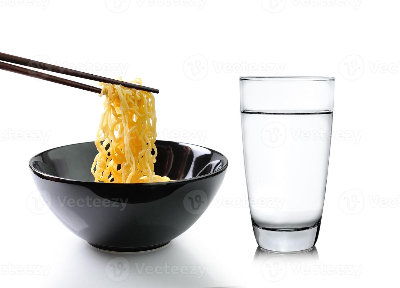 Bacchette che tengono le tagliatelle e un bicchiere d'acqua isolato su sfondo bianco foto