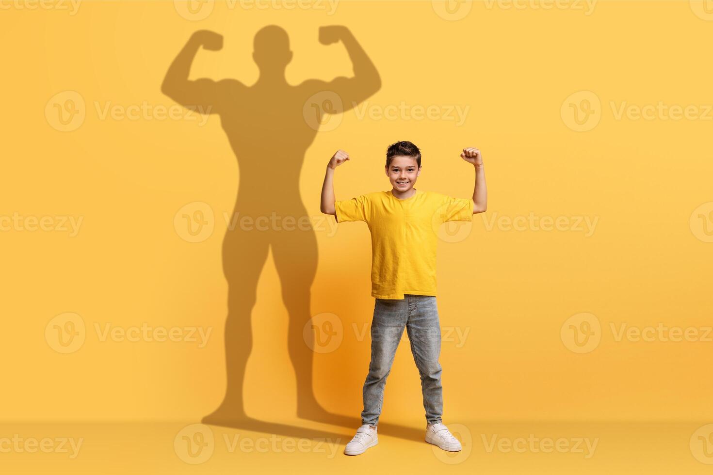 un entusiasta giovane ragazzo nel un' giallo camicia si flette il suo braccia con fiducia foto