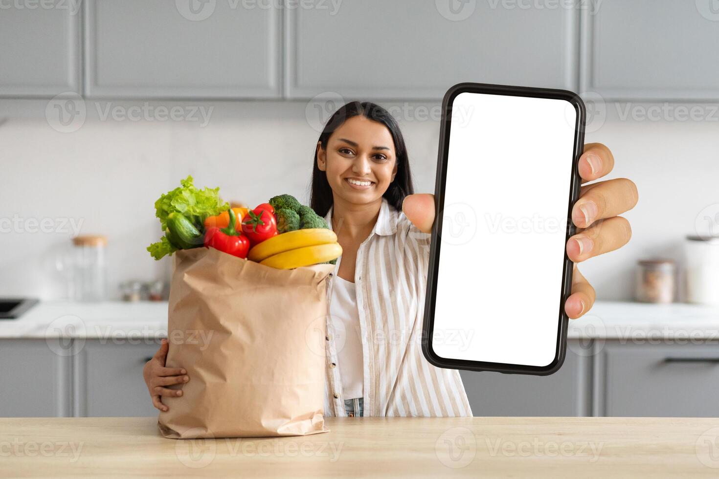 contento giovane indiano donna ordine drogheria in linea, mostrando smartphone foto