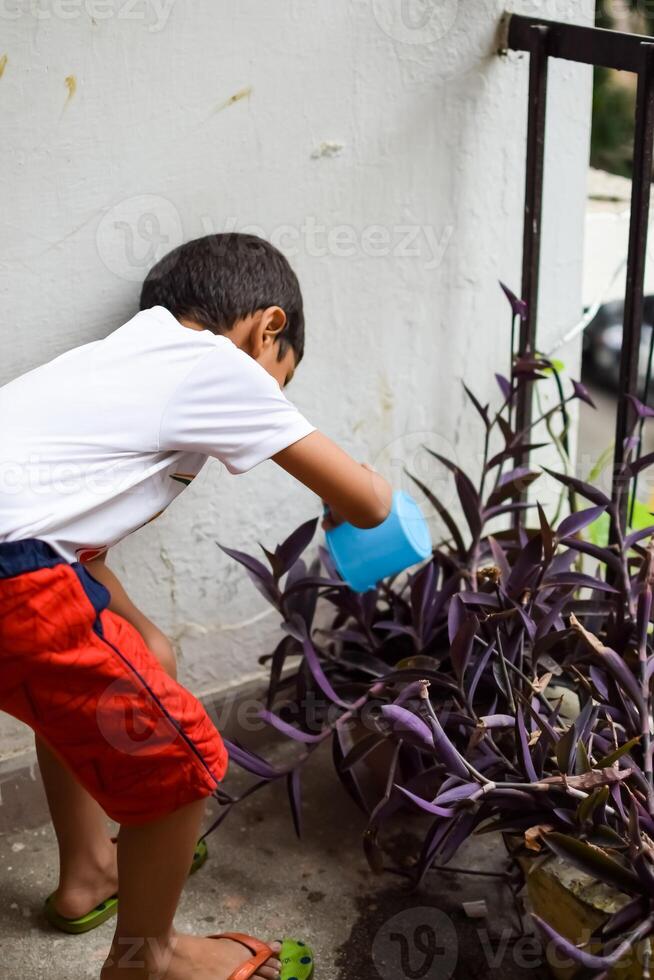 carino 5 anno vecchio asiatico poco ragazzo è irrigazione il pianta nel il pentole collocato a Casa balcone, amore di dolce poco ragazzo per il madre natura durante irrigazione in impianti, ragazzo piantare foto