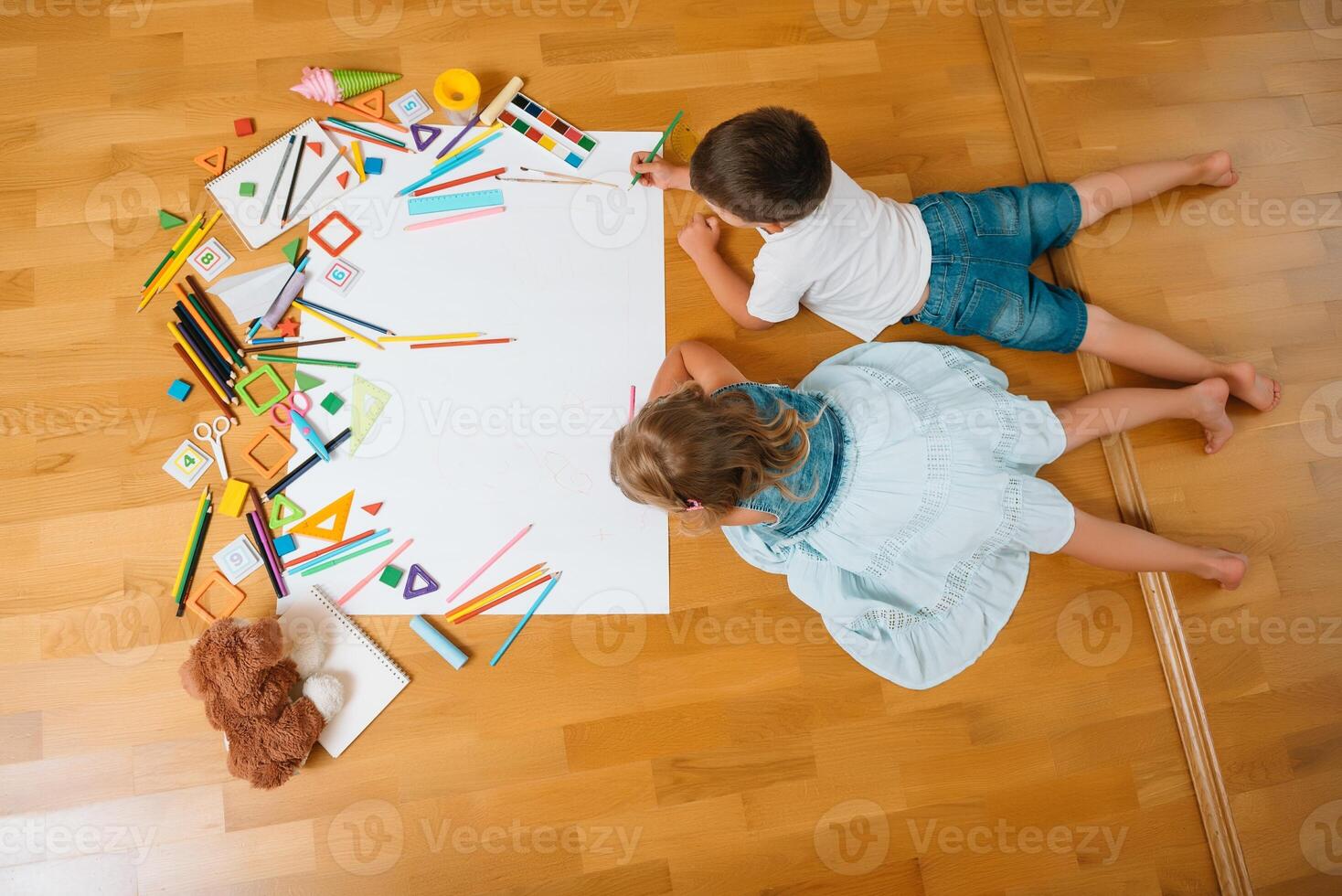 bambini disegno su pavimento su carta. prescolastico ragazzo e ragazza giocare su pavimento con educativo giocattoli - blocchi, treno, Ferrovia, aereo. giocattoli per prescolastico e asilo. bambini a casa o asilo nido. superiore Visualizza. foto