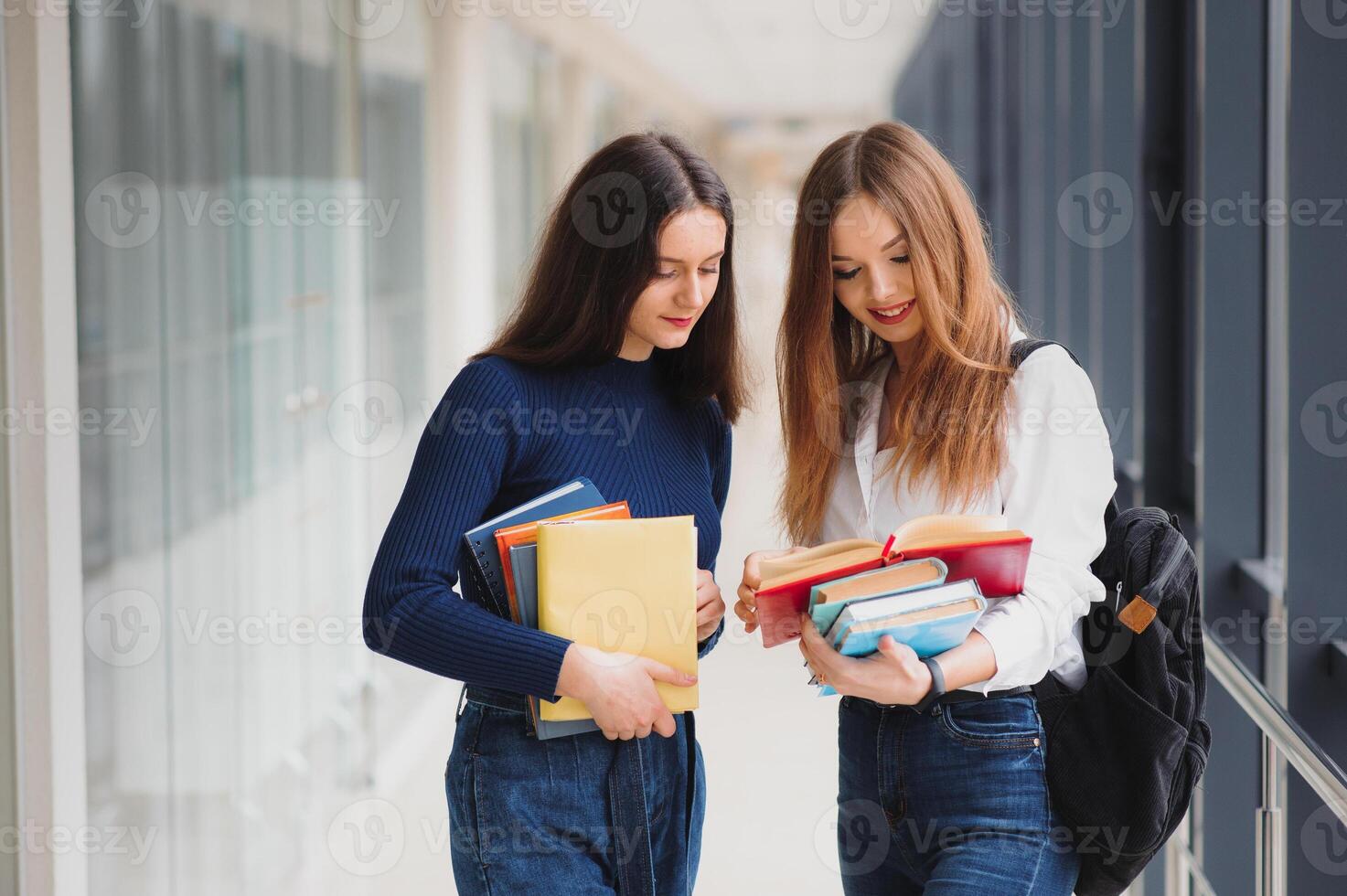 Due giovane femmina studenti in piedi con libri e borse nel il corridoio Università A proposito di ogni Altro. foto