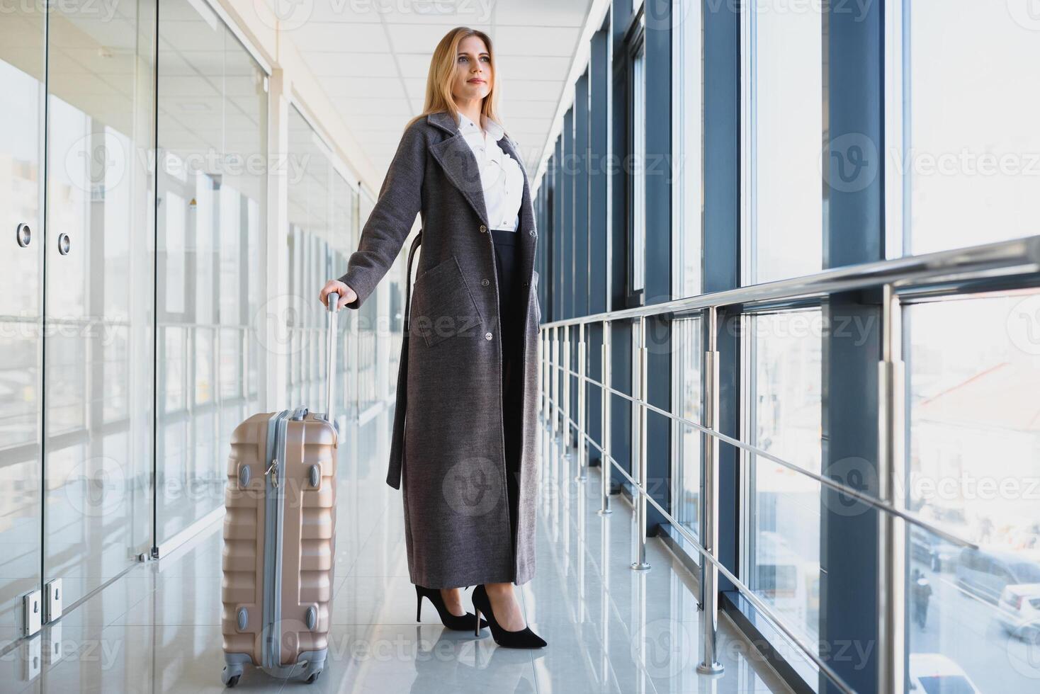 attraente giovane donna con viaggio valigia in piedi su secondo pavimento di aeroporto in attesa camera azione foto