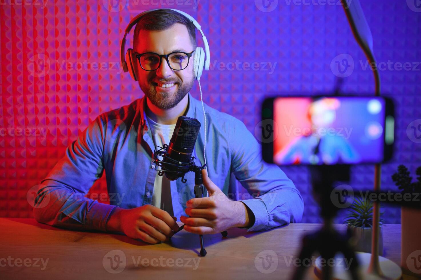 vlogger utilizzando smartphone per film Podcast nel studio. blogger con mobile Telefono, microfono e cuffie le riprese video per sociale media emittente carriera. foto