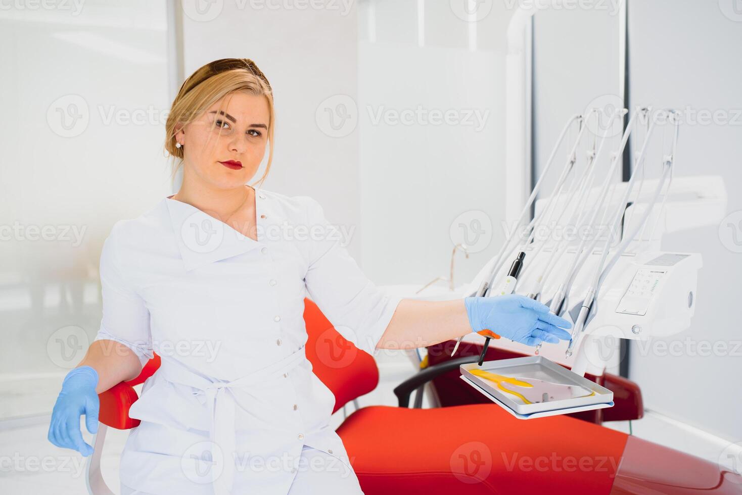 le persone, medicinale, stomatologia e assistenza sanitaria concetto - contento giovane femmina dentista con utensili al di sopra di medico ufficio sfondo foto