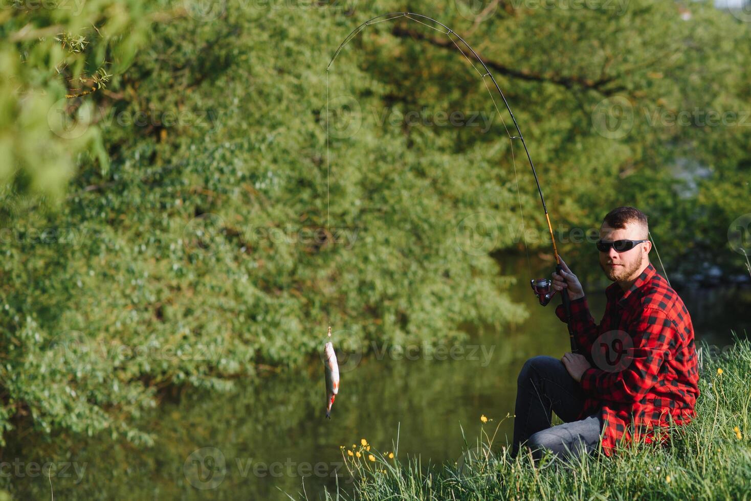 pescatore uomo pesca con Filatura asta su un' fiume banca, rotazione pesca, preda pesca foto