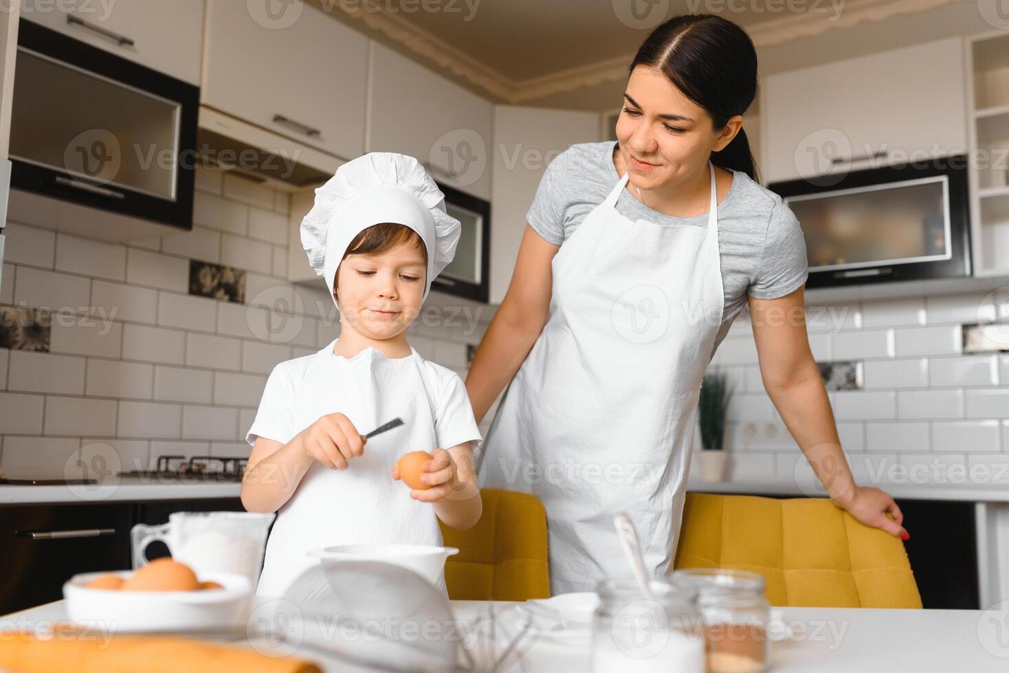 contento madre e sua poco figlio tremante crudo uova nel ciotola prima fabbricazione Impasto per fatti in casa Pasticcino nel il cucina foto