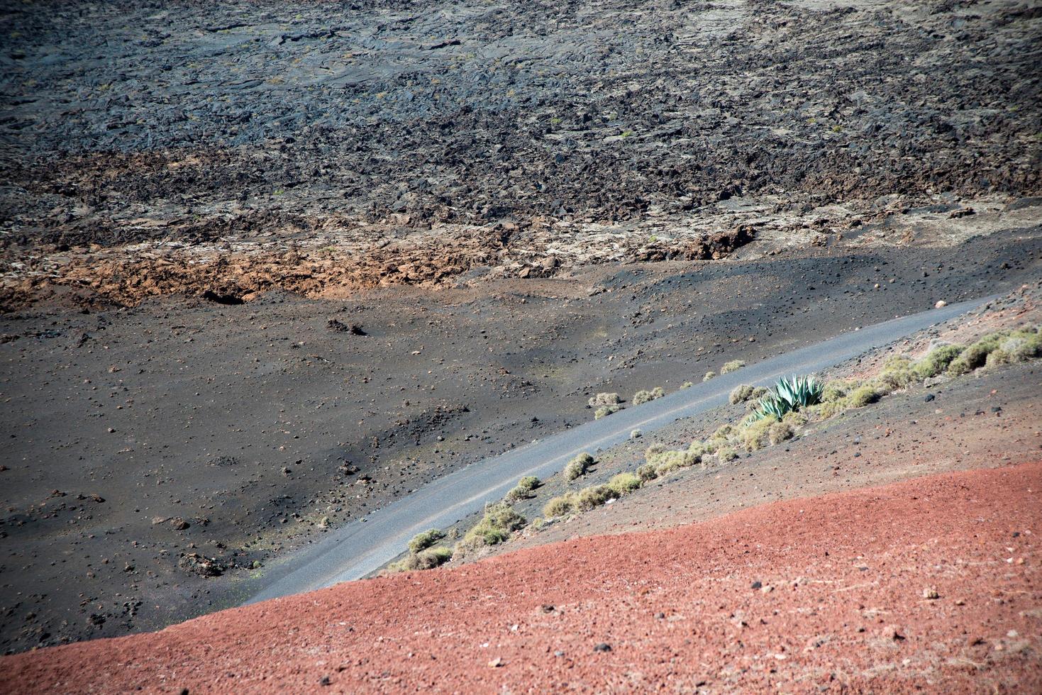 strada che attraversa una bellissima area vulcanica a lanzarote. rocce laviche, sabbia rossa e cactus. isole canarie, spagna foto