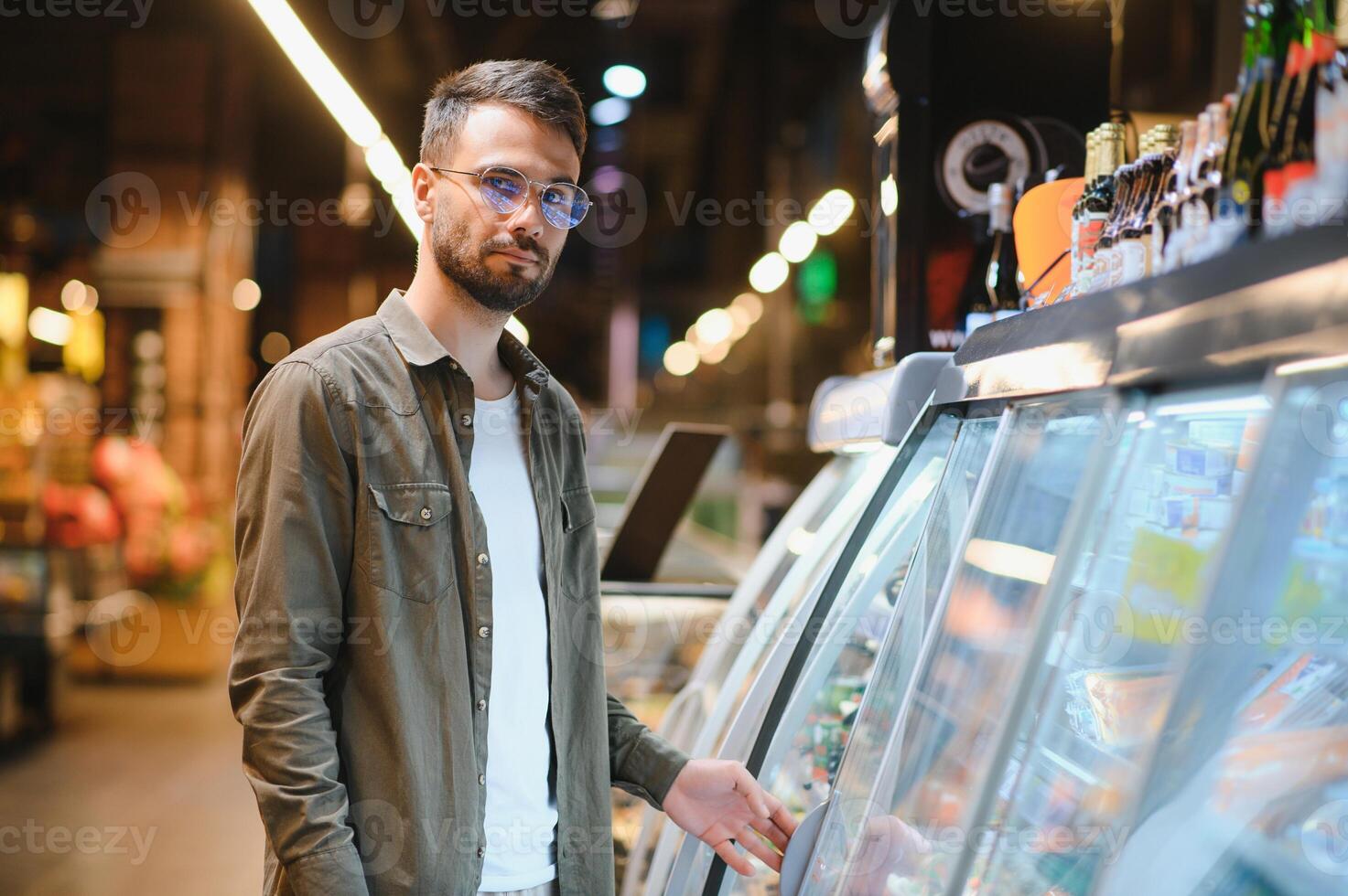 giovane uomo acquisto drogheria a il supermercato. altro i clienti nel sfondo. consumismo concetto. foto