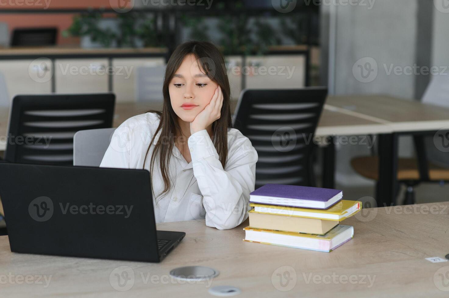 un' bellissimo caucasico femmina alunno è studiando nel Università a distanza. lei è seduta con un' il computer portatile e un' bloc notes e concentrato è Guardando un' video conferenza lezione foto