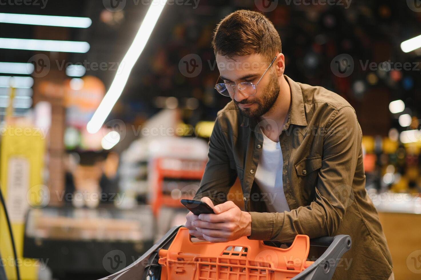 Presto testo durante acquisti. bello giovane uomo Tenere mobile Telefono e sorridente mentre in piedi nel un' cibo memorizzare foto