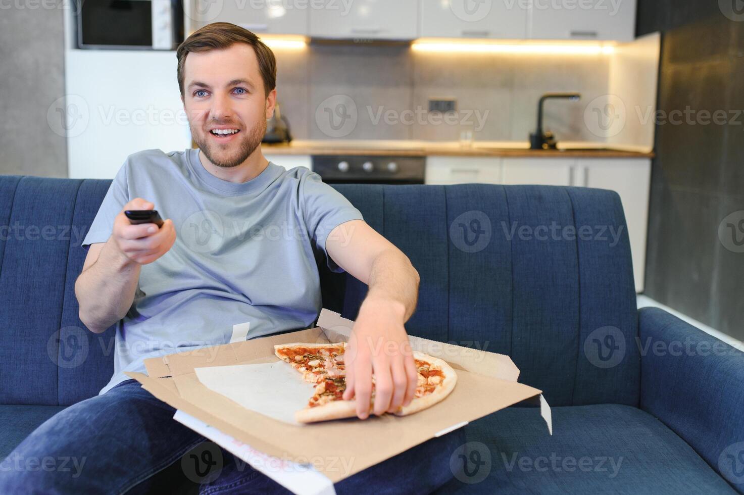 contento giovane uomo potabile birra e mangiare Pizza quando Guardando gioco su tv a casa foto