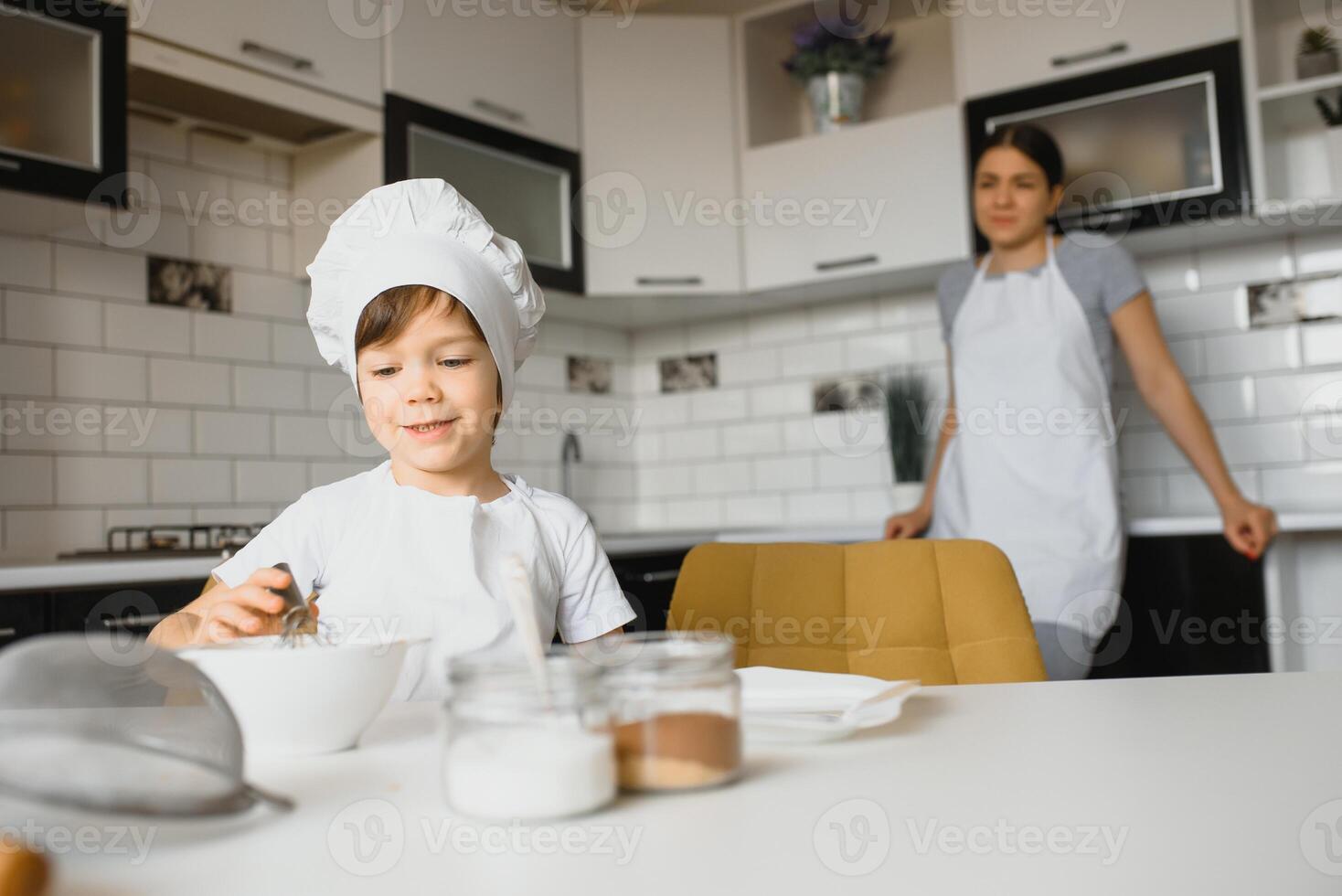 un' giovane e bellissimo madre è preparazione cibo a casa nel il cucina, lungo con sua poco figlio foto