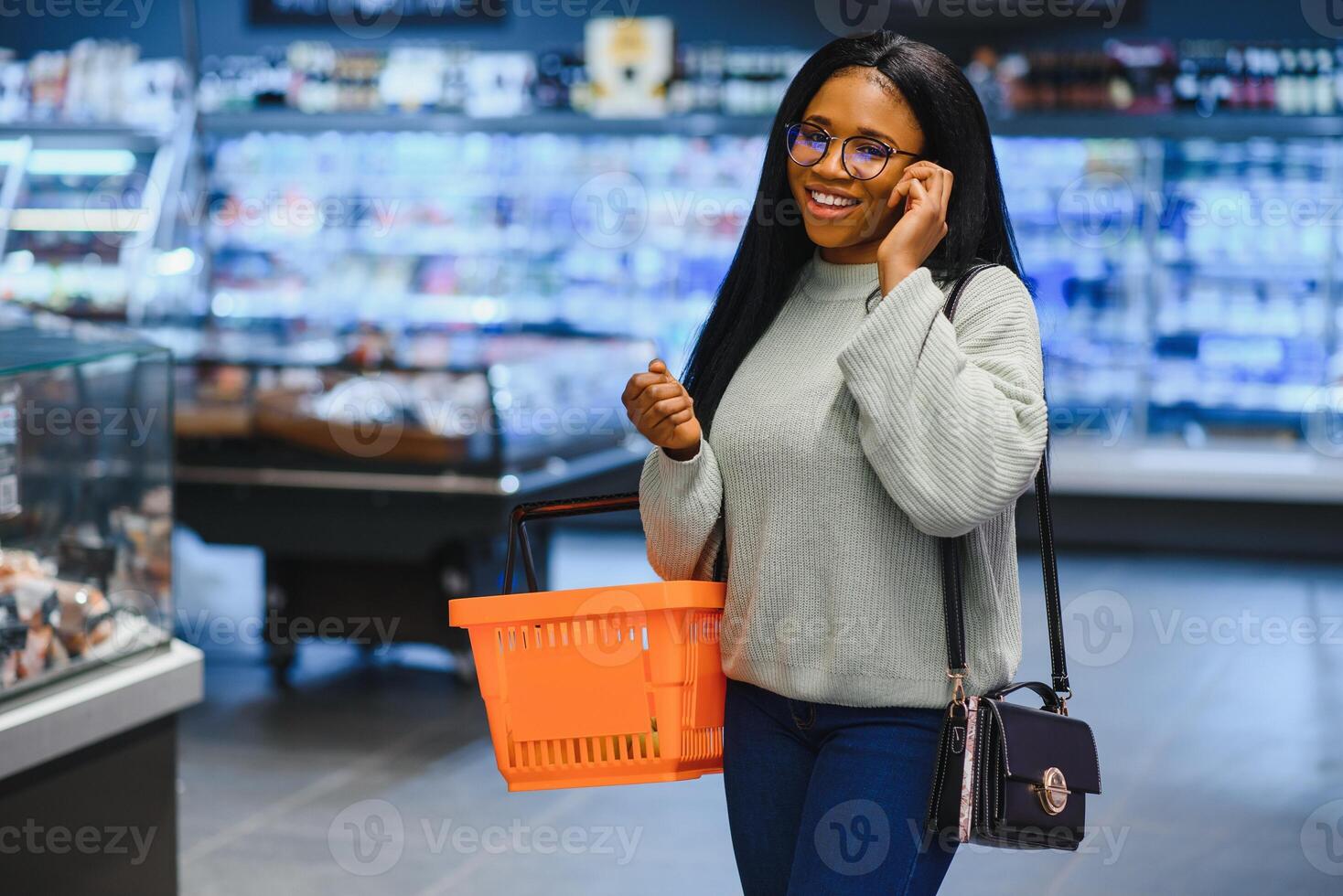 africano americano donna con shopping carrello carrello nel il supermercato memorizzare parlare su mobile Telefono foto