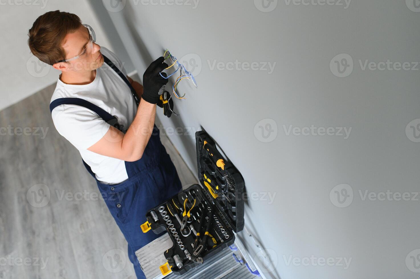 elettricista costruttore a opera, installazione di prese e interruttori. professionale nel tuta da lavoro con un elettricista attrezzo. contro il sfondo di il riparazione luogo. foto