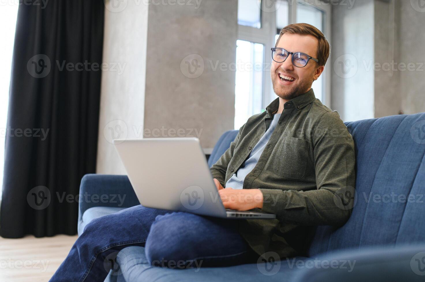 uomini Lavorando su il computer portatile computer nel il suo camera. casa opera o studia, libero professionista concetto. giovane uomo seduta rilassato su divano con il computer portatile. moderno uomo d'affari utilizzando il computer portatile. foto