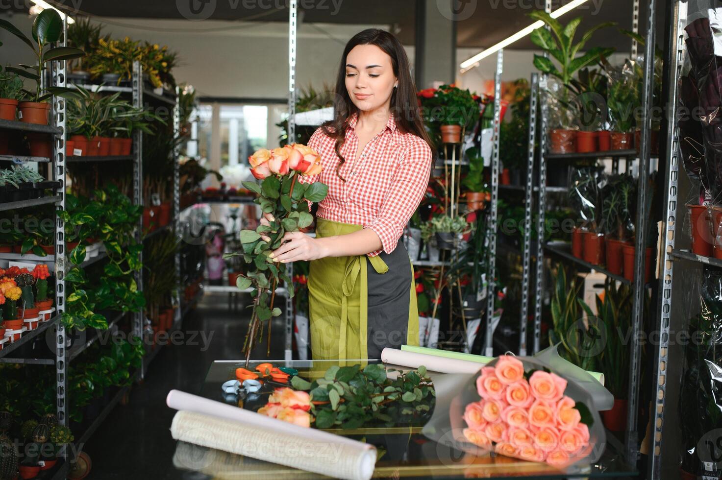 carino ragazza fioraio raccoglie un' mazzo di Rose nel un' fiore negozio. un' bellissimo fioraio crea un' composizione di fiori. ragazza tagli fiori e rimuove stantio le foglie foto