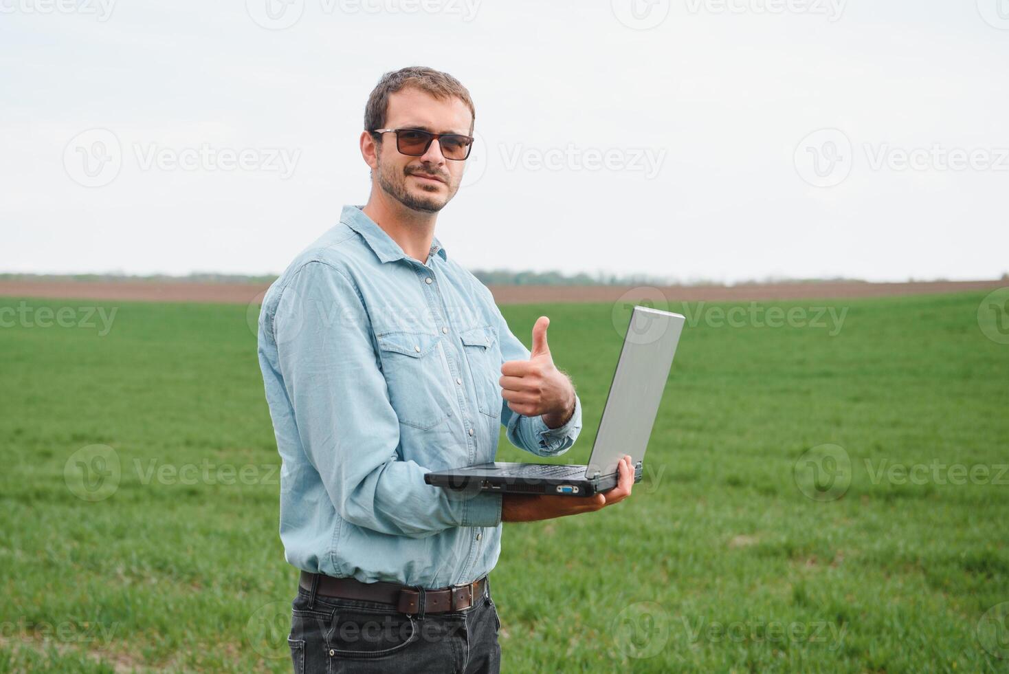 uomo contadino Lavorando su un' il computer portatile nel il campo. agronomo esamina il verde germoglio inverno Grano. foto