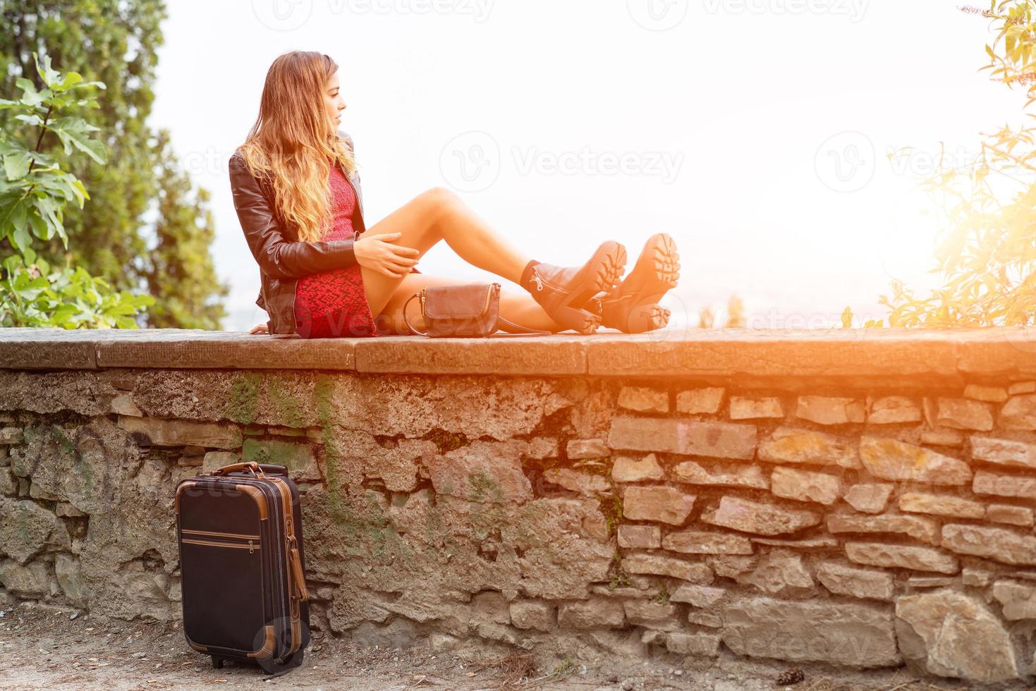 ragazza al sole su un muro con la valigia in attesa. foto