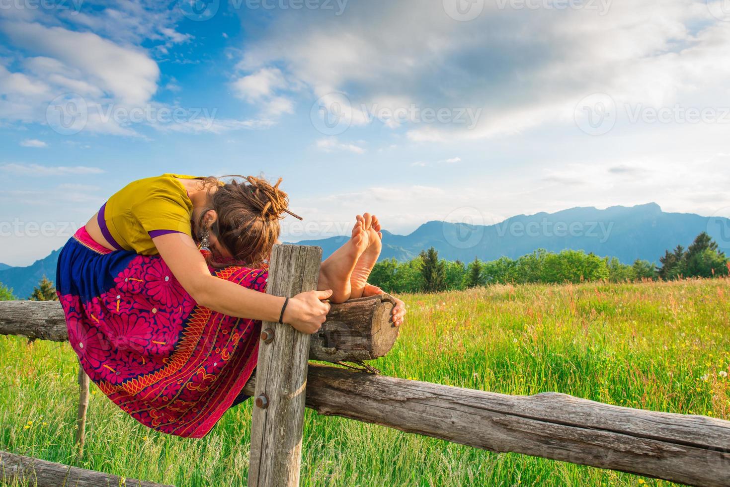 ragazza casual si rilassa facendo stretching e yoga da solo in montagna sopra un recinto in un bellissimo prato di primavera. foto