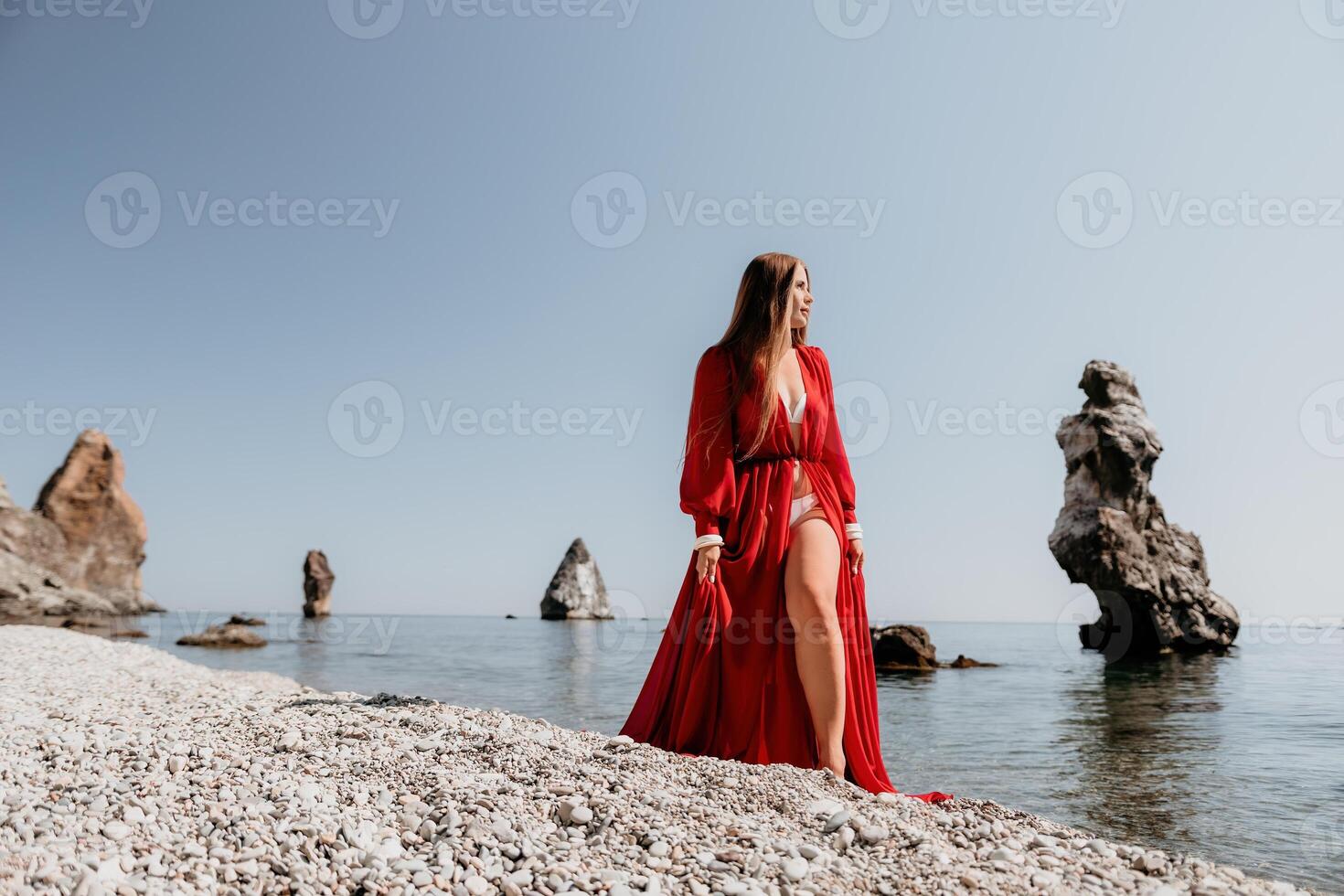 donna viaggio mare. contento turista nel rosso vestito godere assunzione immagine all'aperto per ricordi. donna viaggiatore in posa su il roccia a mare baia circondato di vulcanico montagne, condivisione viaggio avventura viaggio foto