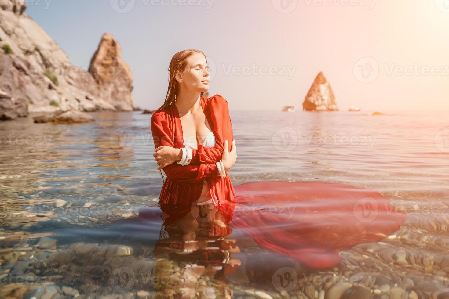 donna viaggio mare. contento turista nel rosso vestito godere assunzione immagine all'aperto per ricordi. donna viaggiatore in posa nel mare spiaggia, circondato di vulcanico montagne, condivisione viaggio avventura viaggio foto