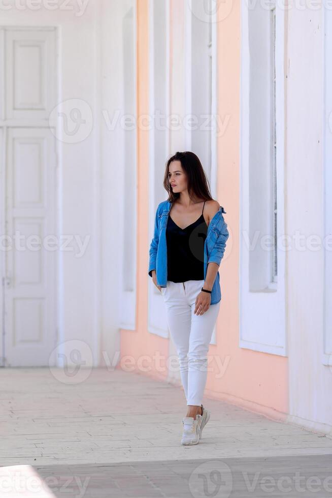 bellissimo ragazza a piedi nel leggero sala con alto cella. girt nel bianca jeans e blu camicia. pieno lunghezza foto. foto