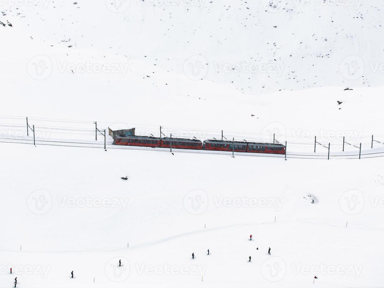 colorato treno in mezzo sciatori nel nevoso Zermatt, Svizzera aereo Visualizza foto