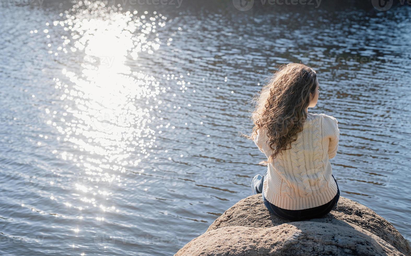 premurosa donna romantica seduta sulla riva del fiume al tramonto in autunno day foto