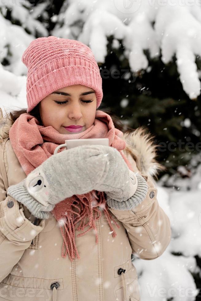 bella donna in abiti invernali caldi che tiene tazza bevendo tè o caffè caldo all'aperto in una giornata nevosa foto