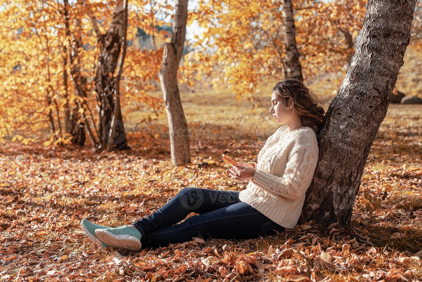 giovane donna premurosa seduta vicino all'albero nella foresta autunnale foto