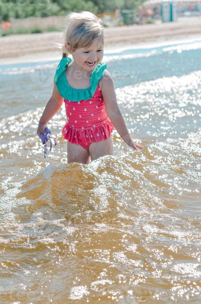 giovane contento bambino ragazza di europeo aspetto età di 4 avendo divertimento nel acqua su il spiaggia ,tropicale estate vocazioni,vacanze.a bambino gode il mare.verticale fotocopia spazio foto