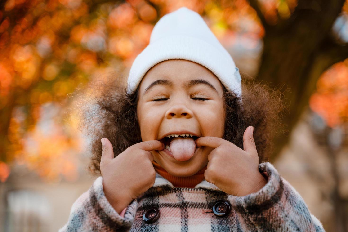 ragazza riccia nera che mostra la sua lingua mentre si prende in giro nel parco autunnale foto